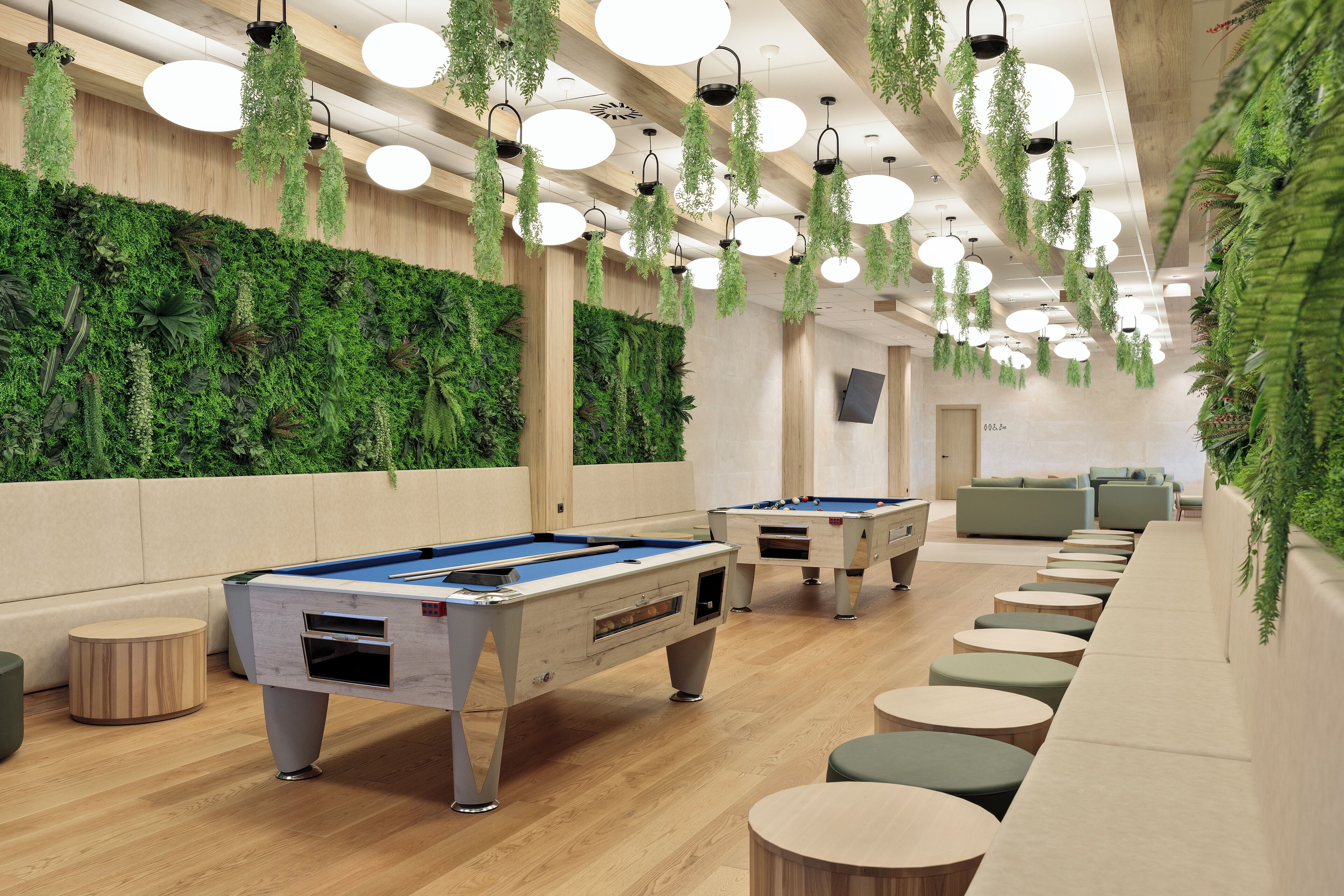 A pool table area with multiple tables, hanging plants, and a wooden ceiling.