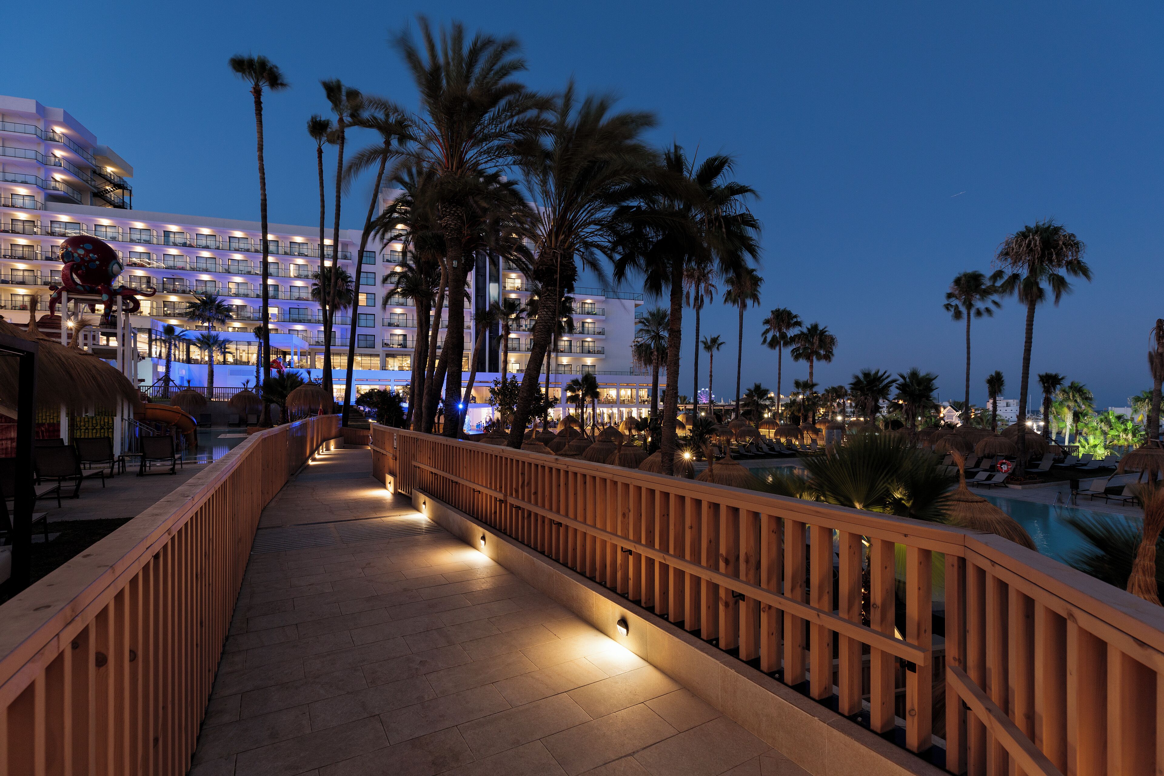 A hotel with a pool area, palm trees, and a wooden walkway.