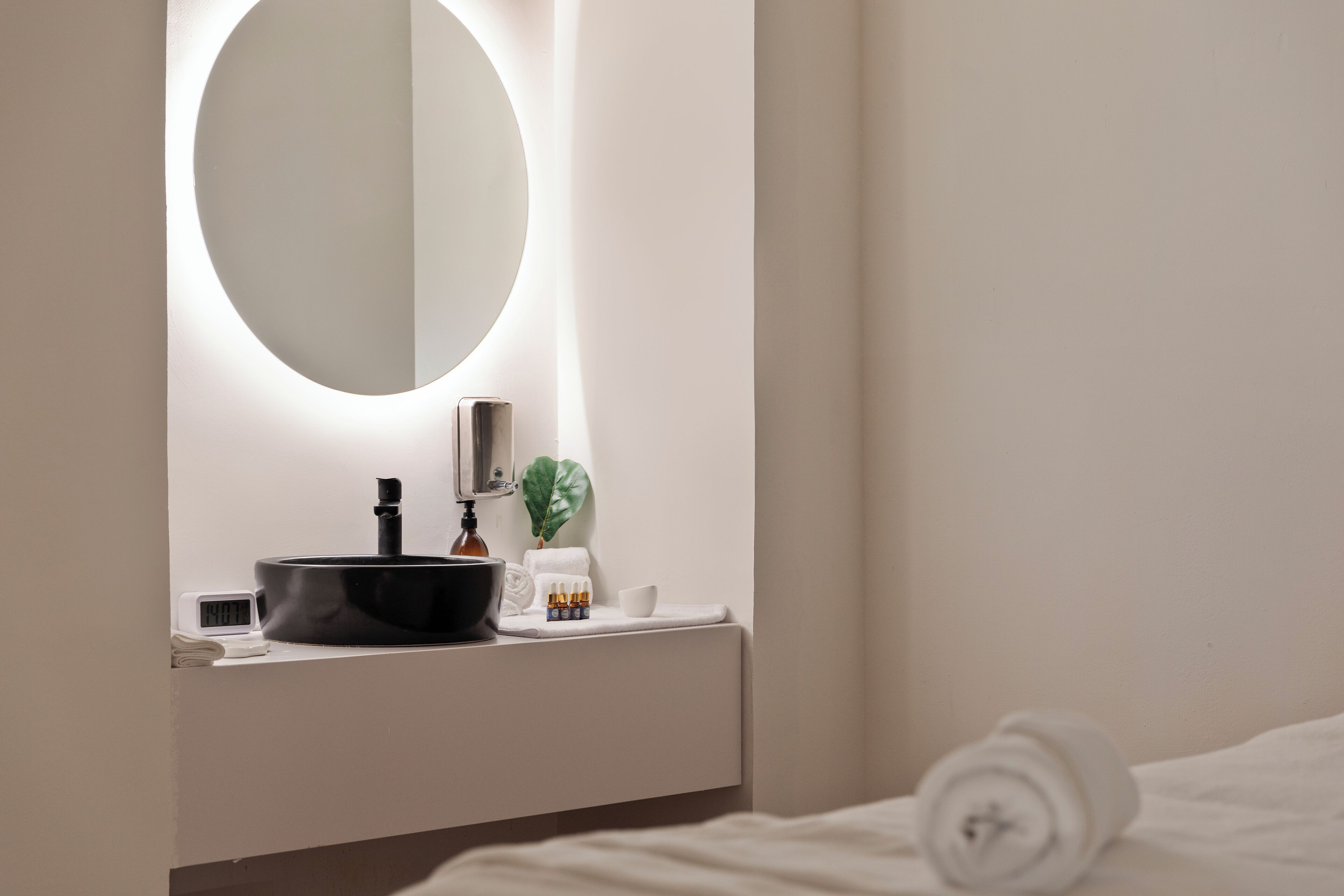 A modern bathroom with a round mirror, a black basin, a small plant, and a white towel on the counter.