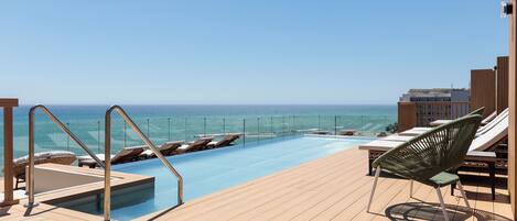Zona de piscina con sillones de descanso y vista al océano.