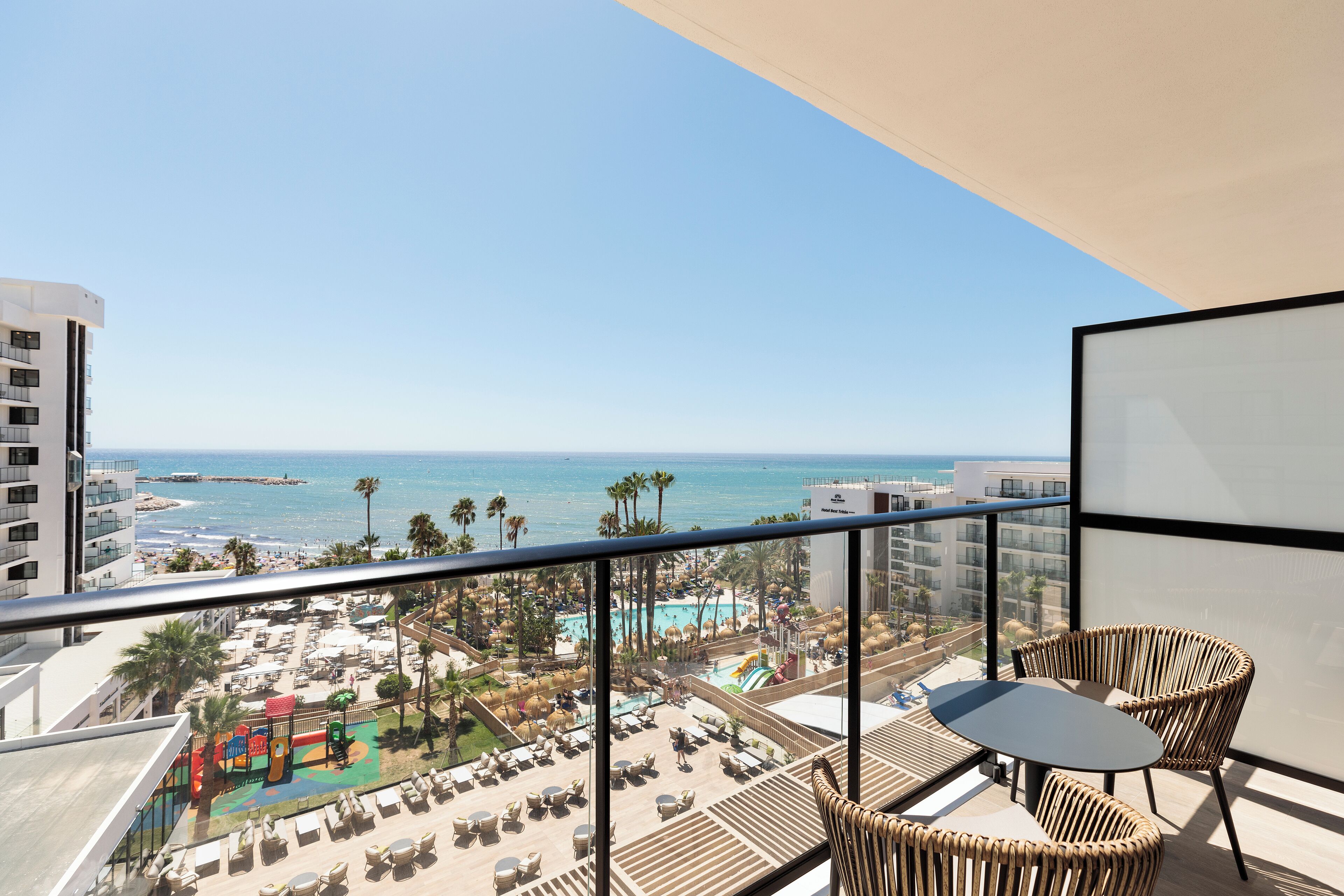 A balcony with a view of a beach resort, including a pool and lounge chairs.