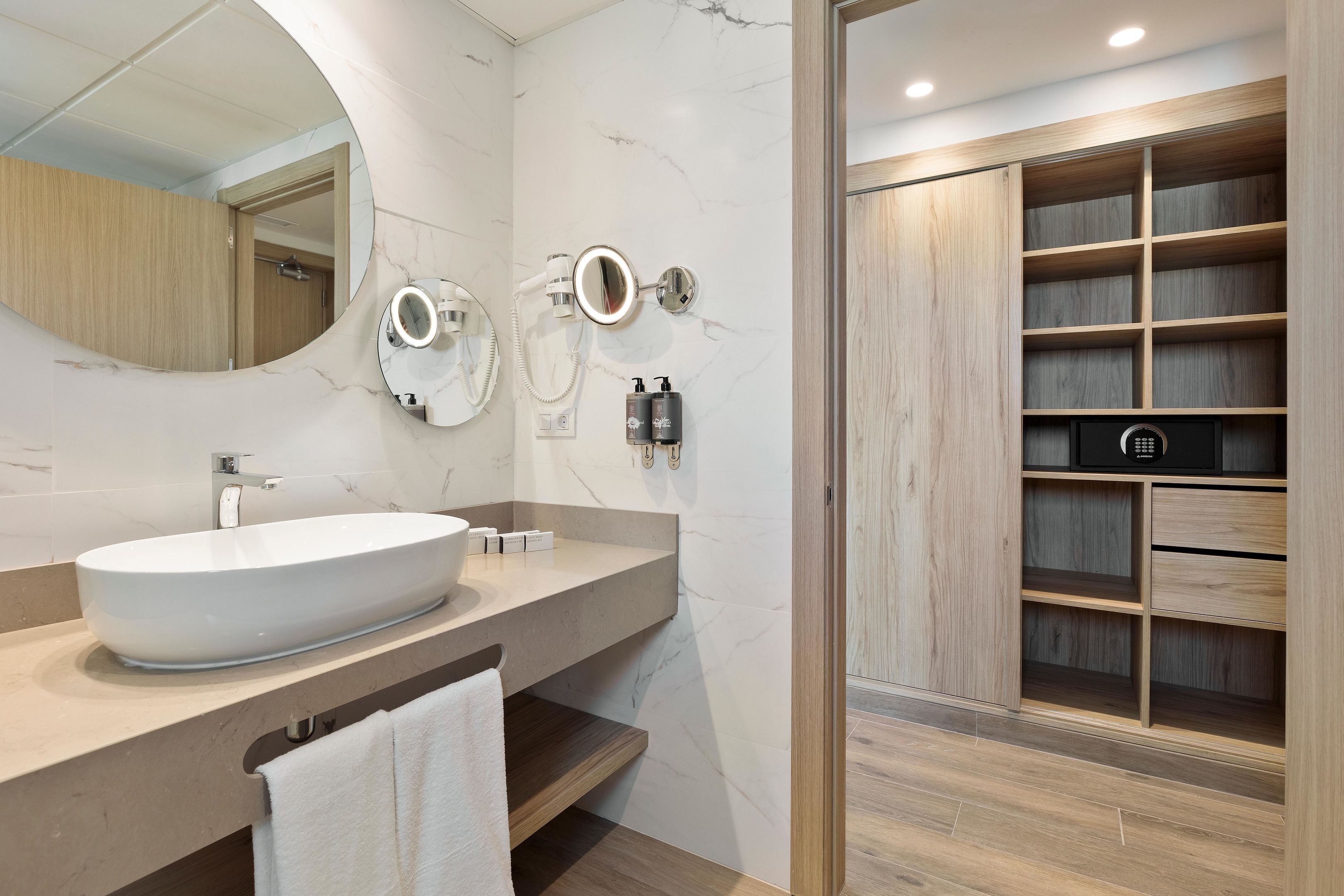A modern bathroom with a large oval sink, a wall-mounted mirror, and a built-in wooden shelving unit.