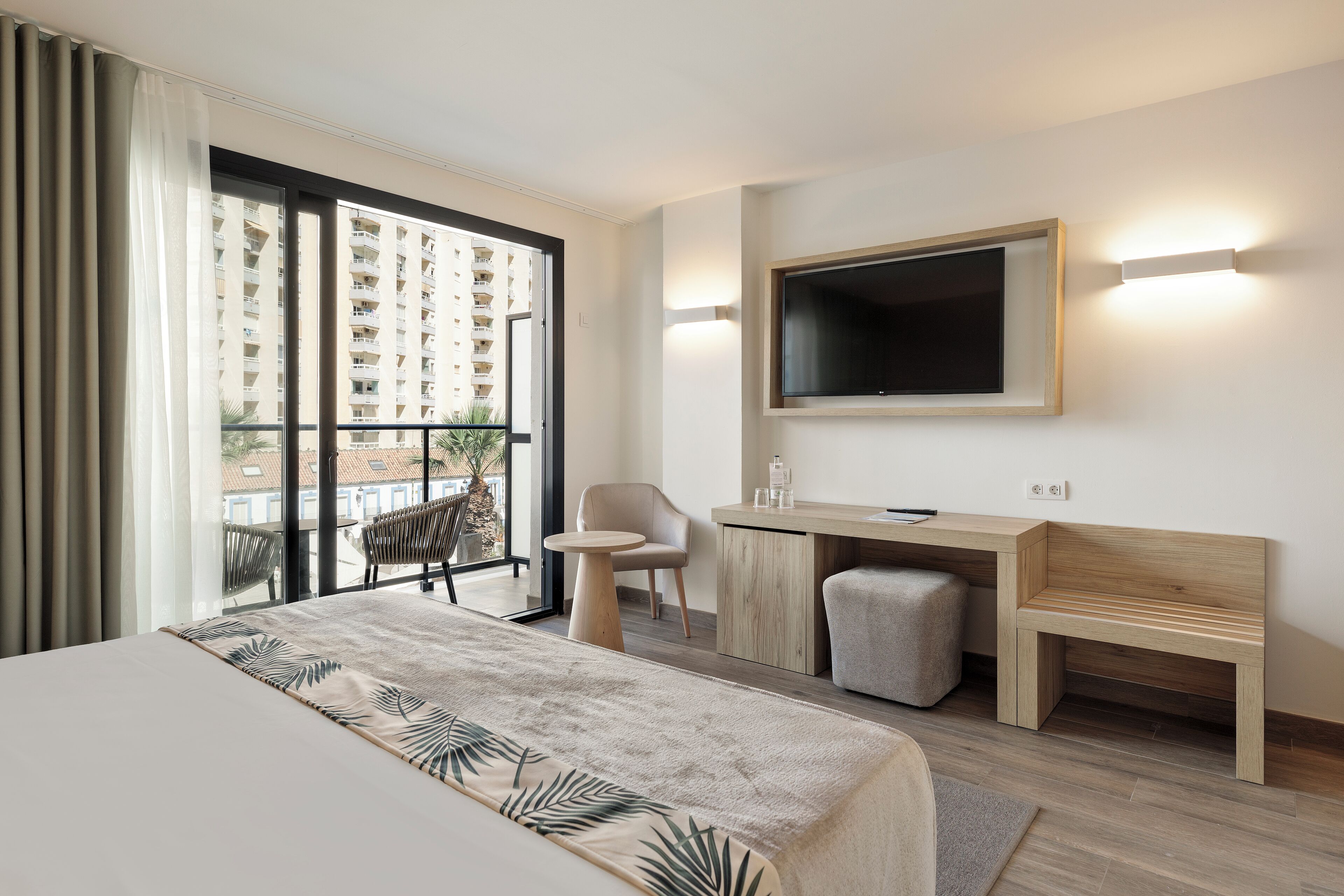 Ein Hotelzimmer mit einem großen Bett, einem Schreibtisch, einem Sessel, einem Fernseher und Blick auf die Stadt.