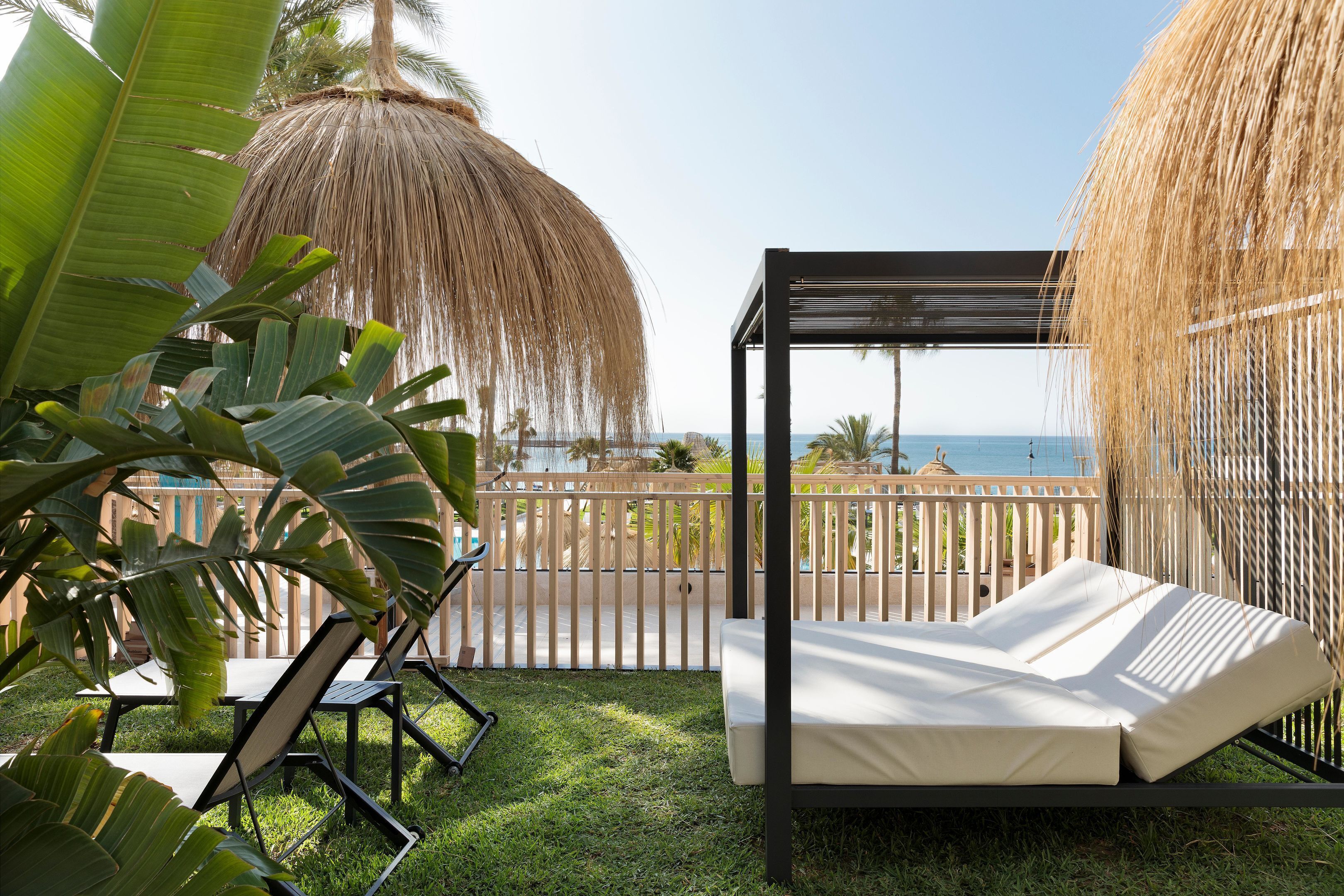 A balcony with a bed, lounge chairs, and a view of the sea.