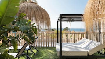 A balcony with a bed, lounge chairs, and a view of the sea.
