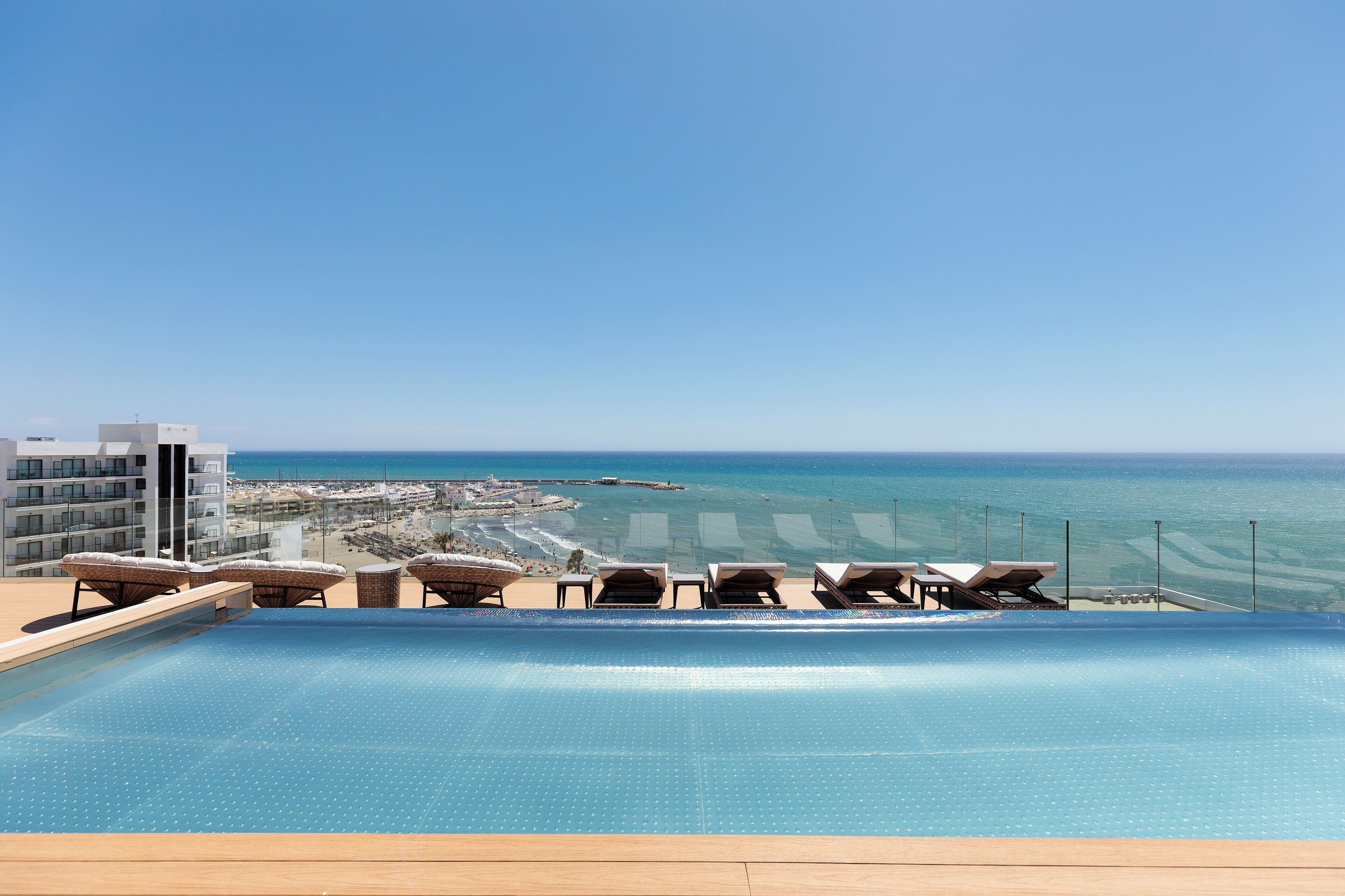 A pool area with lounge chairs and a view of the beach and ocean.