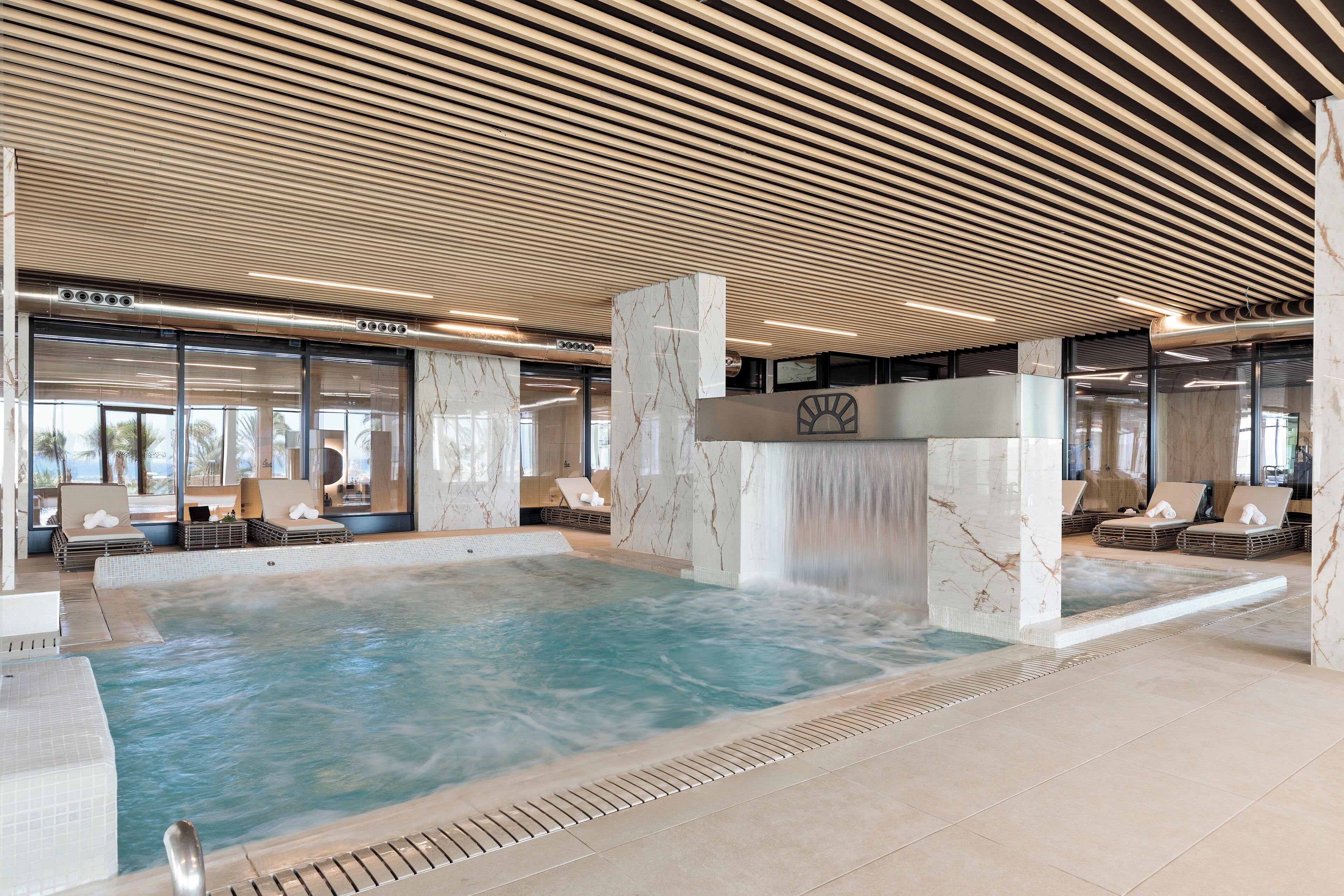 Una amplia piscina interior con sillones de descanso y una cascada.