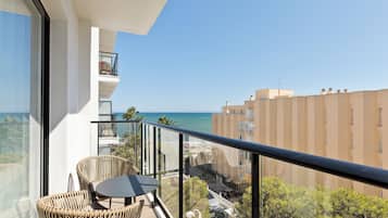 Un balcón con sillas de mimbre y una mesa, con vistas a la costa, edificios y vegetación.