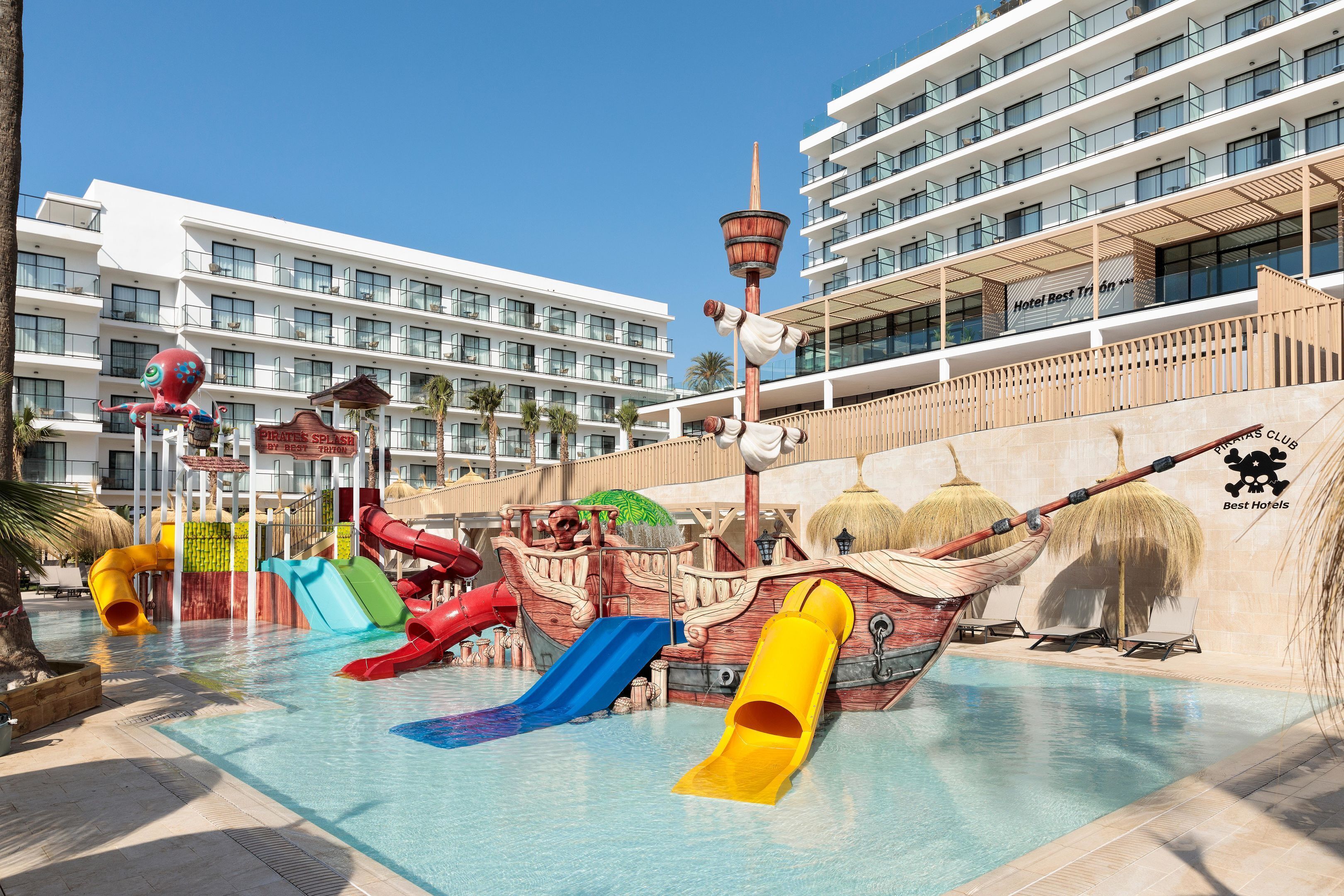 Un parque acuático con toboganes y temática de barco pirata, rodeado de edificios de hotel.