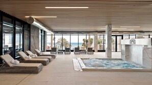 A modern indoor pool area with lounge chairs, a hot tub, and large windows offering a view of the ocean. - Hotel Best Tritón (Benalmádena)