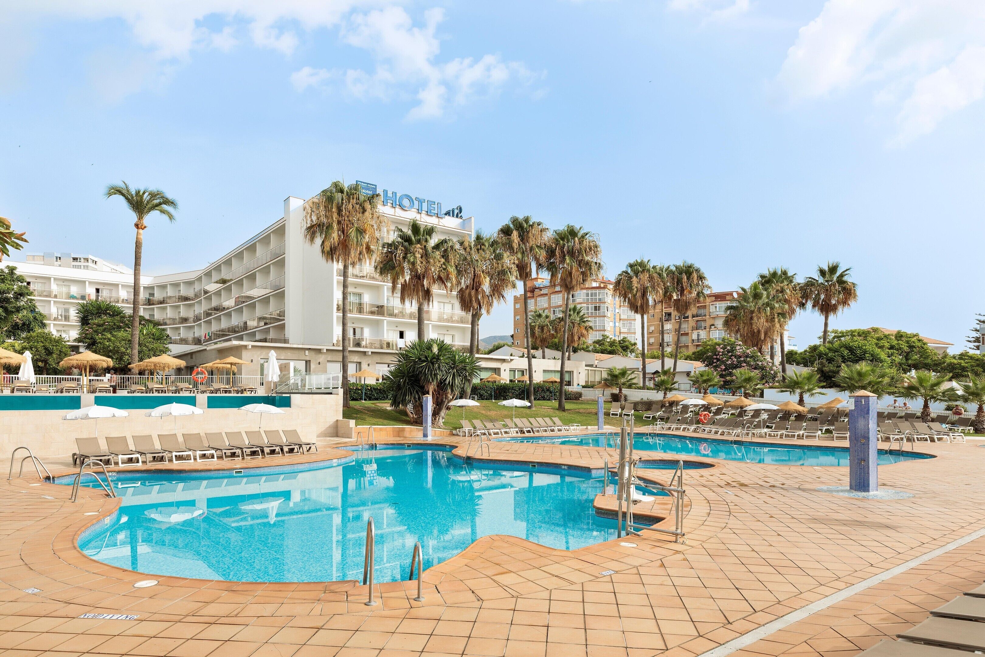 Un hotel con piscina, palmeras y cielo despejado.