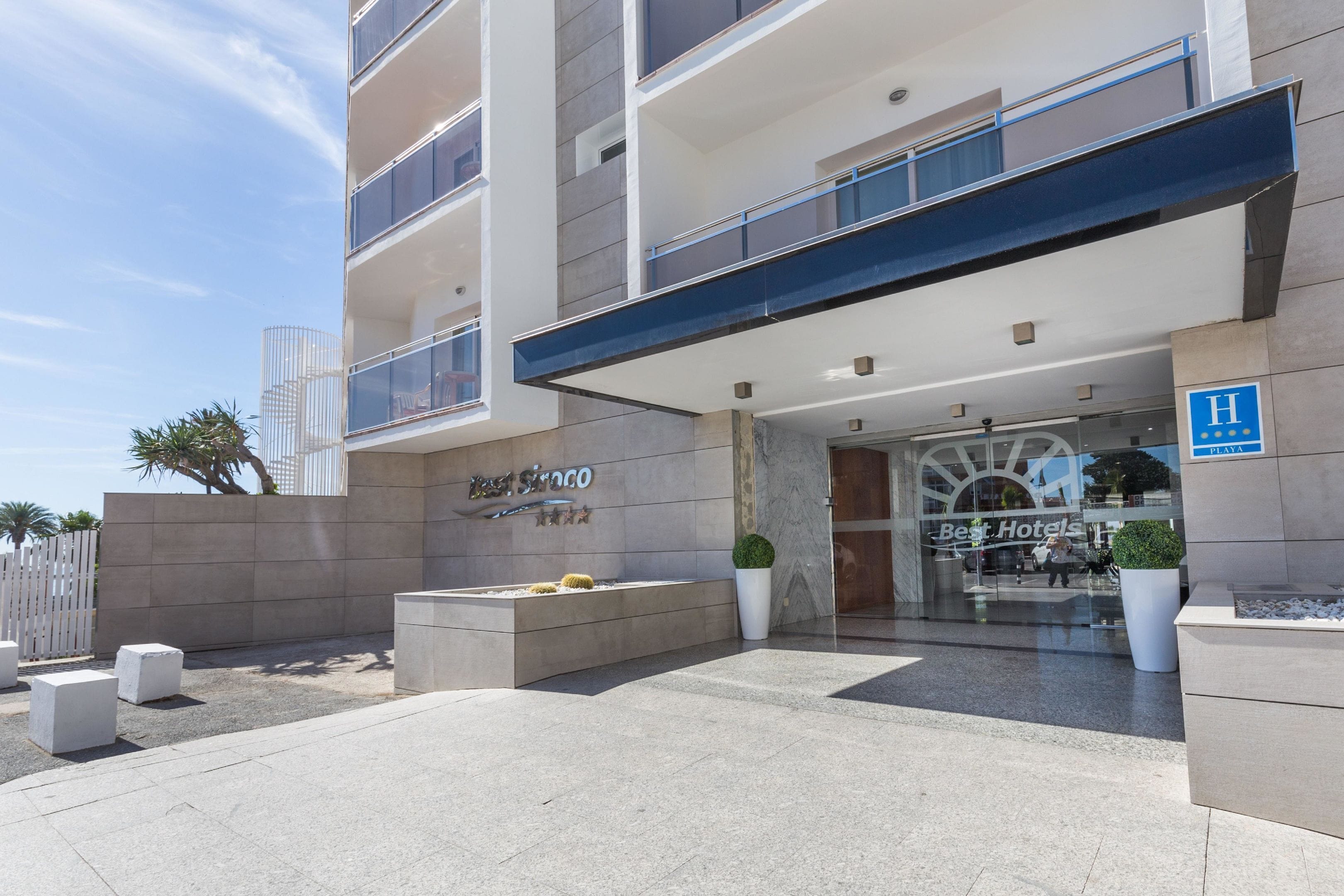 Una entrada de hotel con diseño moderno, que presenta un llamativo cartel que dice 'Best Hotels' y un logotipo 'Best' en la fachada.