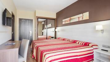 Una habitación de hotel con una cama grande, un escritorio, una silla, un televisor y un espejo.