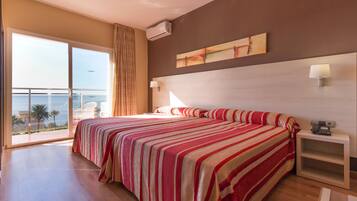 Habitación de hotel con una cama grande, una mesita de noche, una lámpara de pared y vistas al mar a través de una puerta corrediza.