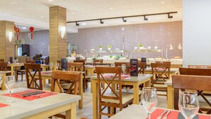 Interior de restaurante con mesas y sillas de madera, manteles individuales rojos y pared de ladrillo al fondo.