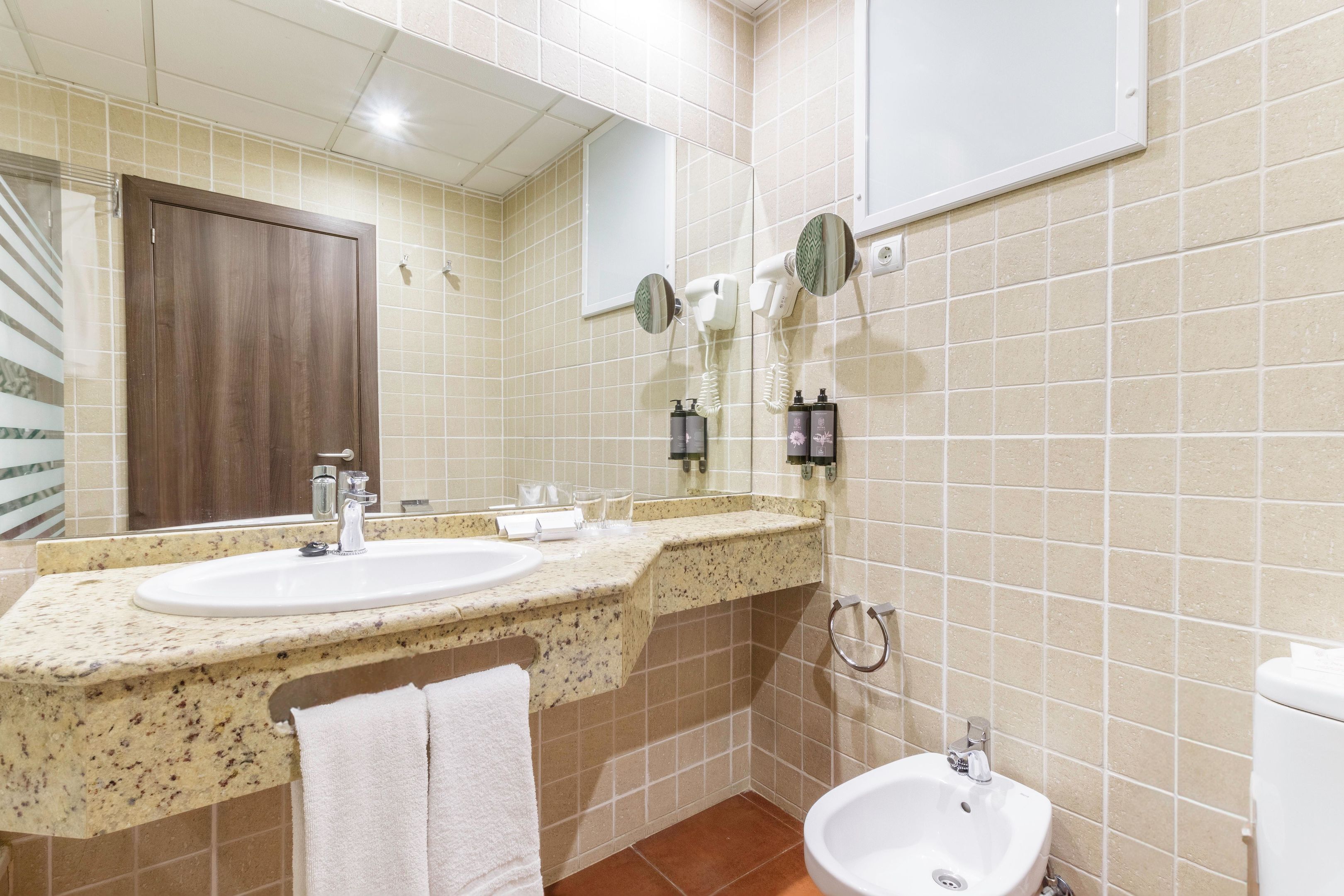 Een badkamer met een wastafel, spiegel, haardroger en een toilet met douchefunctie.