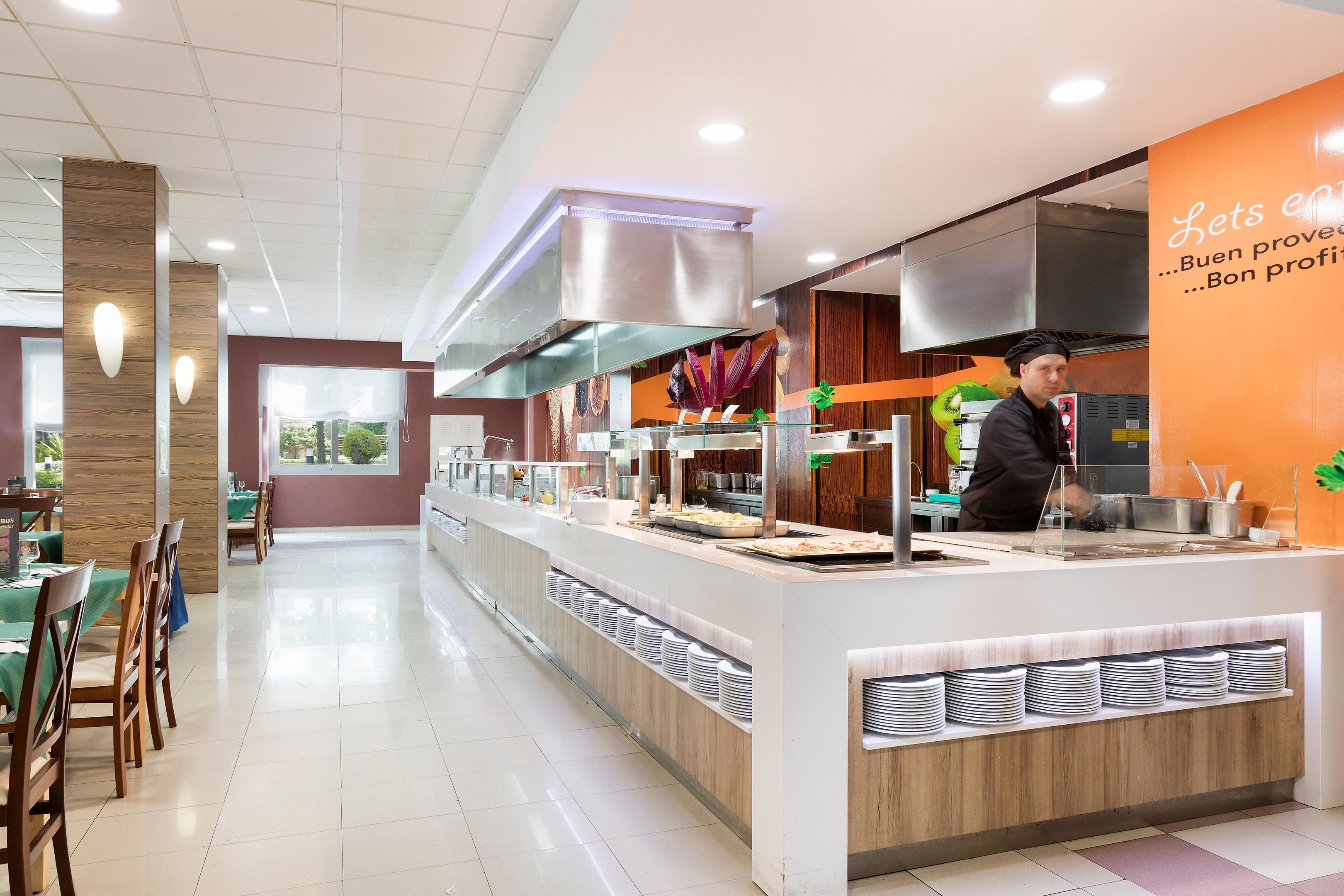 Un restaurante moderno con una barra de buffet, un chef preparando comida y un interior limpio y bien iluminado.