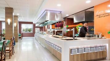 Un restaurante moderno con una barra de buffet, un chef preparando comida y un interior limpio y bien iluminado.