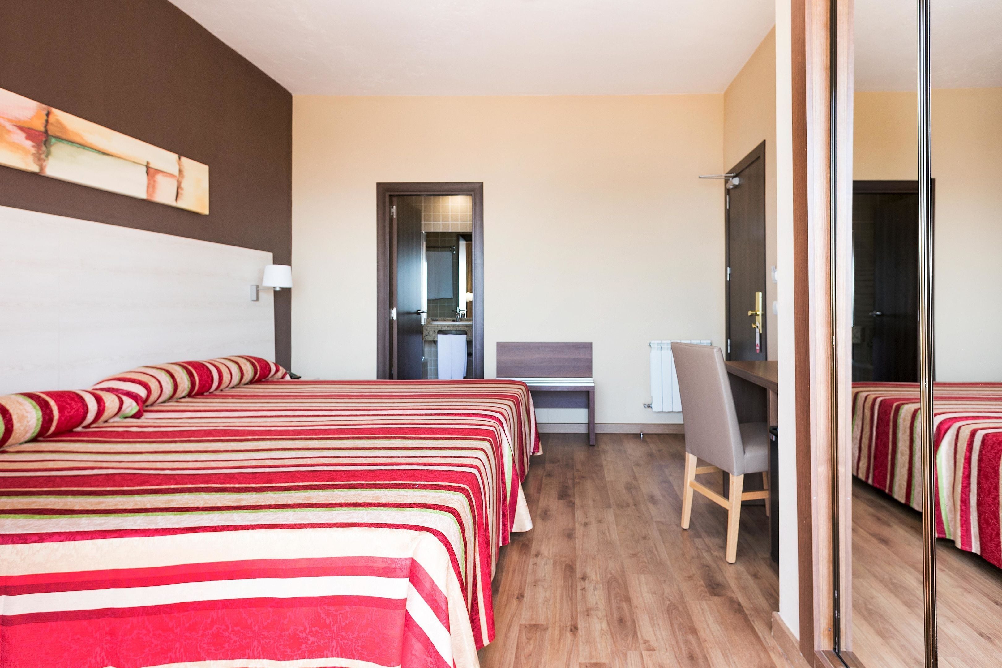 Una habitación de hotel con dos camas, un escritorio, una silla y un espejo.