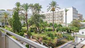 Un hotel con jardín en la azotea, palmeras y un edificio blanco con balcones.