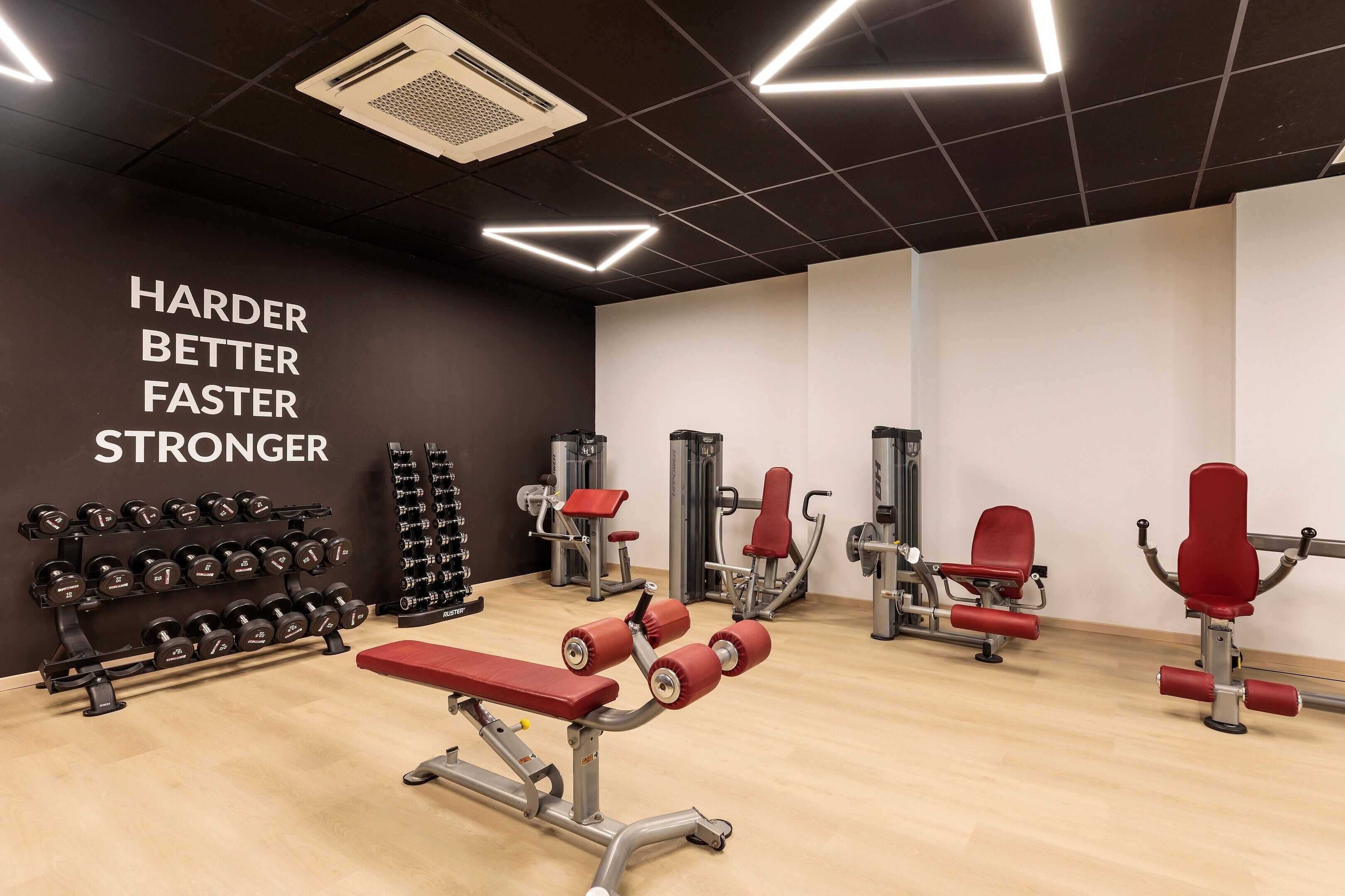 Une salle de sport équipée de divers appareils d’exercice, un mur orné de citations motivantes et un plancher en bois.