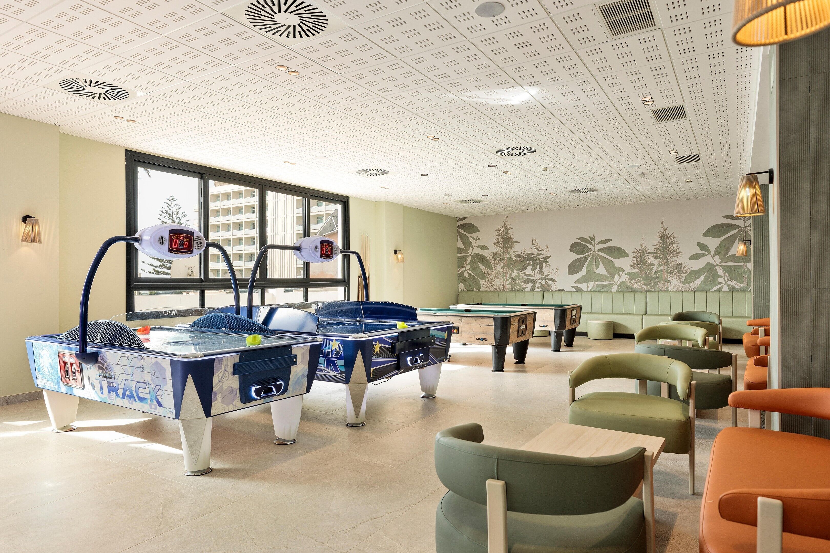 Una sala de billar con dos mesas de pool, sillas verdes y un techo decorativo.