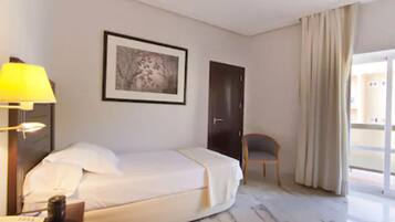 Een hotelkamer met een bed, een bureau met lamp, een stoel, een ingelijste foto aan de muur en een deur.