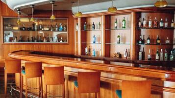 Zona de bar con mostrador de madera, varios taburetes y estantes con botellas.
