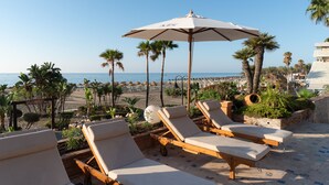 A beachside lounge area with sun loungers and umbrellas, overlooking the sea and palm trees. - Hotel MS Amaragua (Torremolinos)