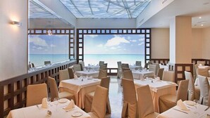 A restaurant with tables set for dining, large windows with a view of the sea, and a skylight above. - Hotel MS Amaragua (Torremolinos)