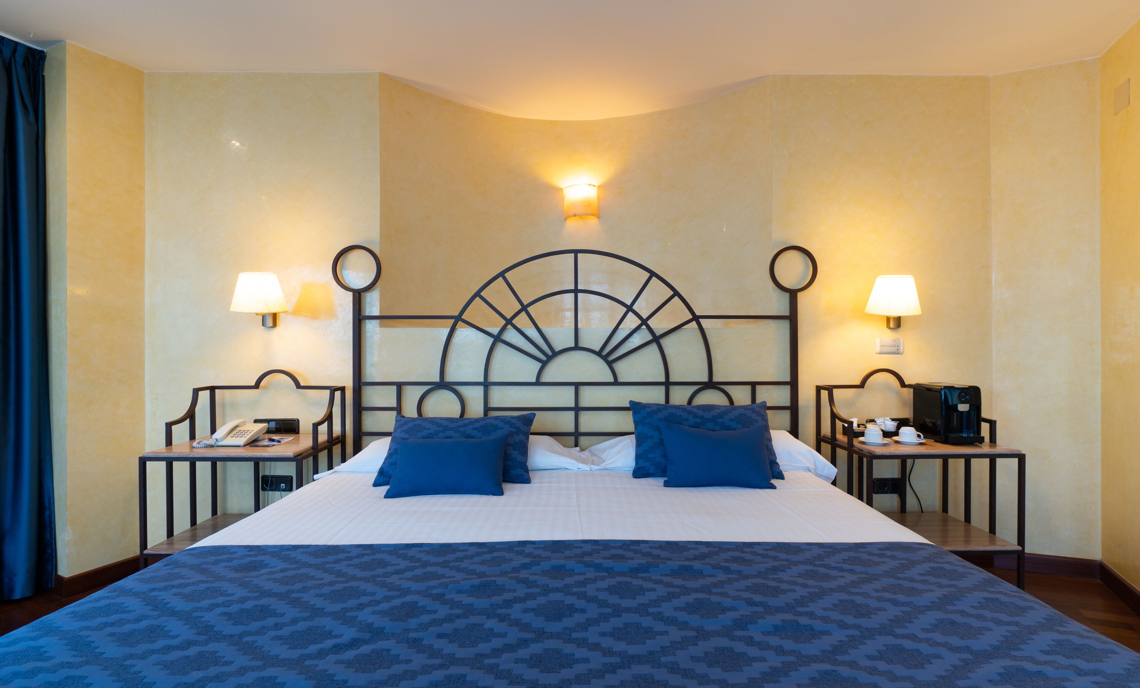 Habitación de hotel con una cama grande, dos mesitas de noche y un cabecero curvado.