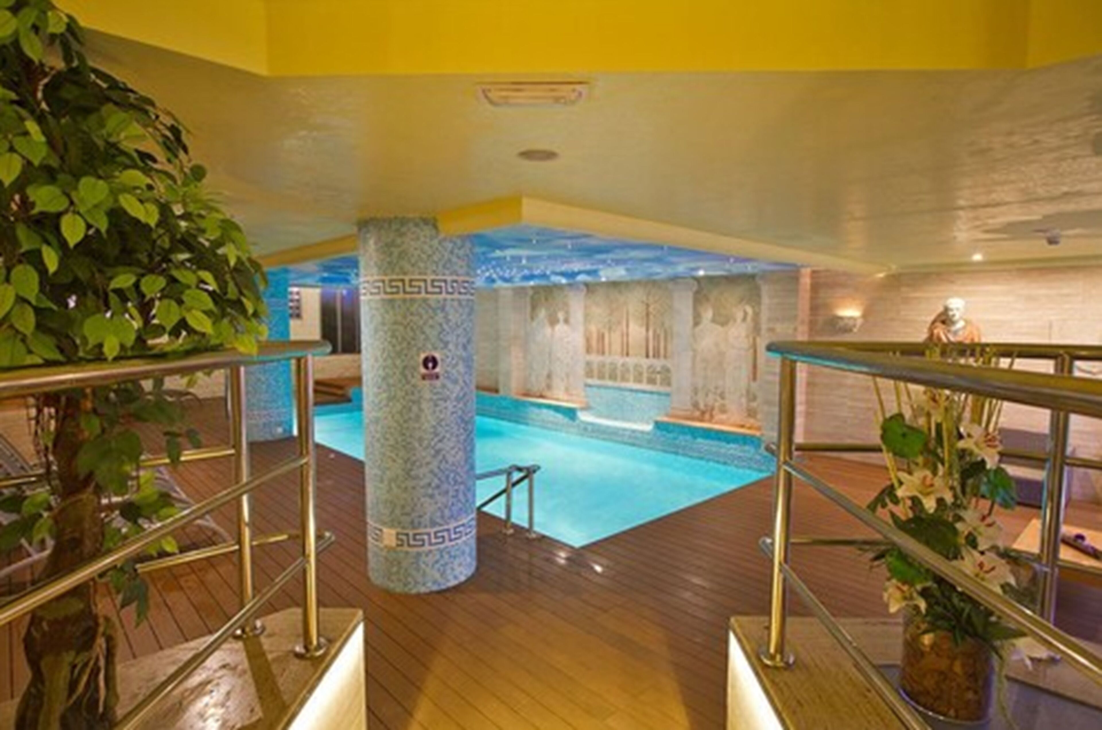 Una piscina interior con cubierta de madera, un pilar de piedra con un logotipo y una estatua al fondo.