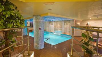 Una piscina interior con cubierta de madera, un pilar de piedra con un logotipo y una estatua al fondo.