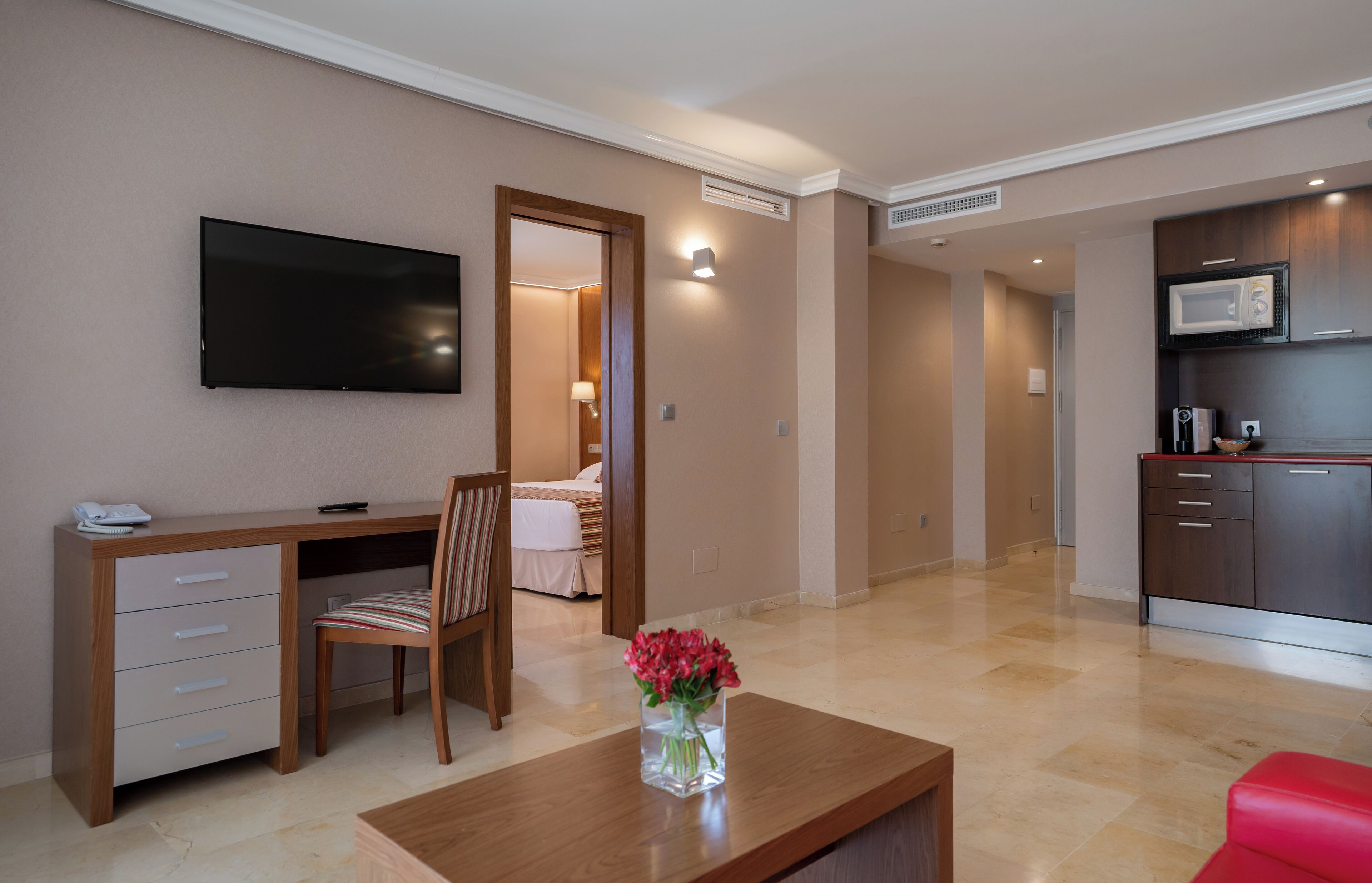 Una sala de estar moderna con un televisor de pantalla plana, un escritorio de madera, una silla, una mesa de centro con un florero y un sofá rojo.