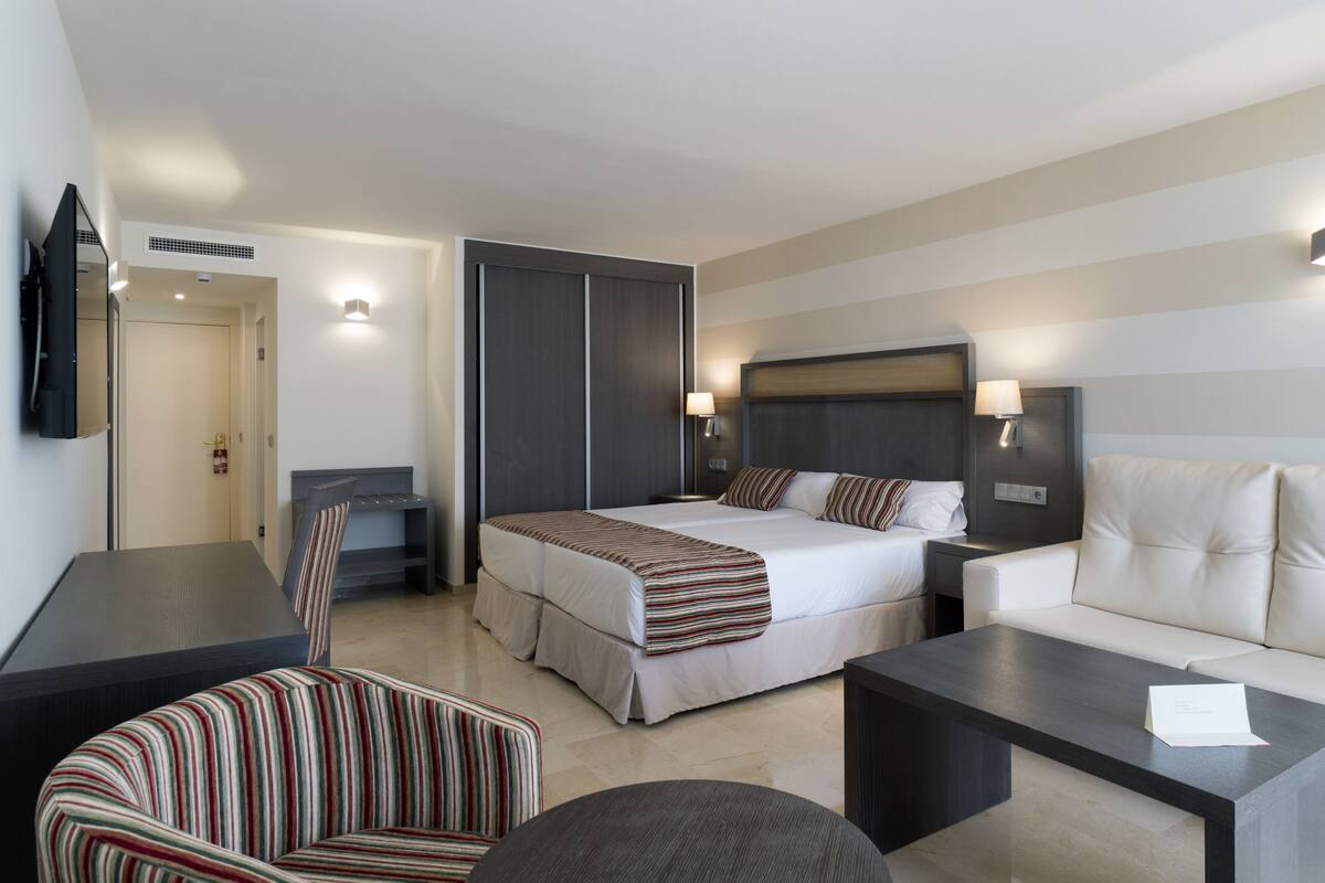 A hotel room with a bed, a sofa, a chair, a coffee table, and a TV.