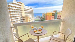 Un balcón con dos sillas y una mesa dispuesta para el desayuno, con vistas a la ciudad y al mar.