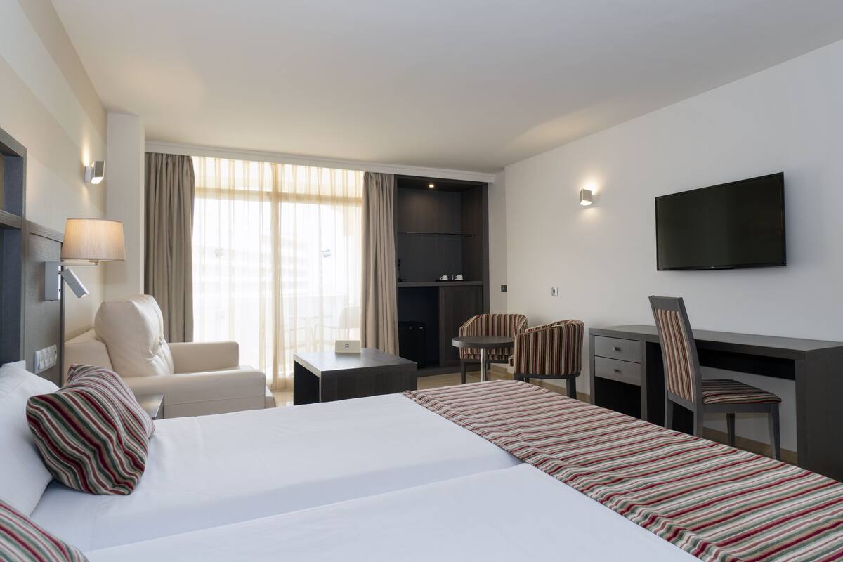 A hotel room with a large bed, a desk, a chair, a television, and a window with curtains.