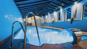 Una piscina interior con cubierta de madera, barandillas de metal y pared de azulejos azules.