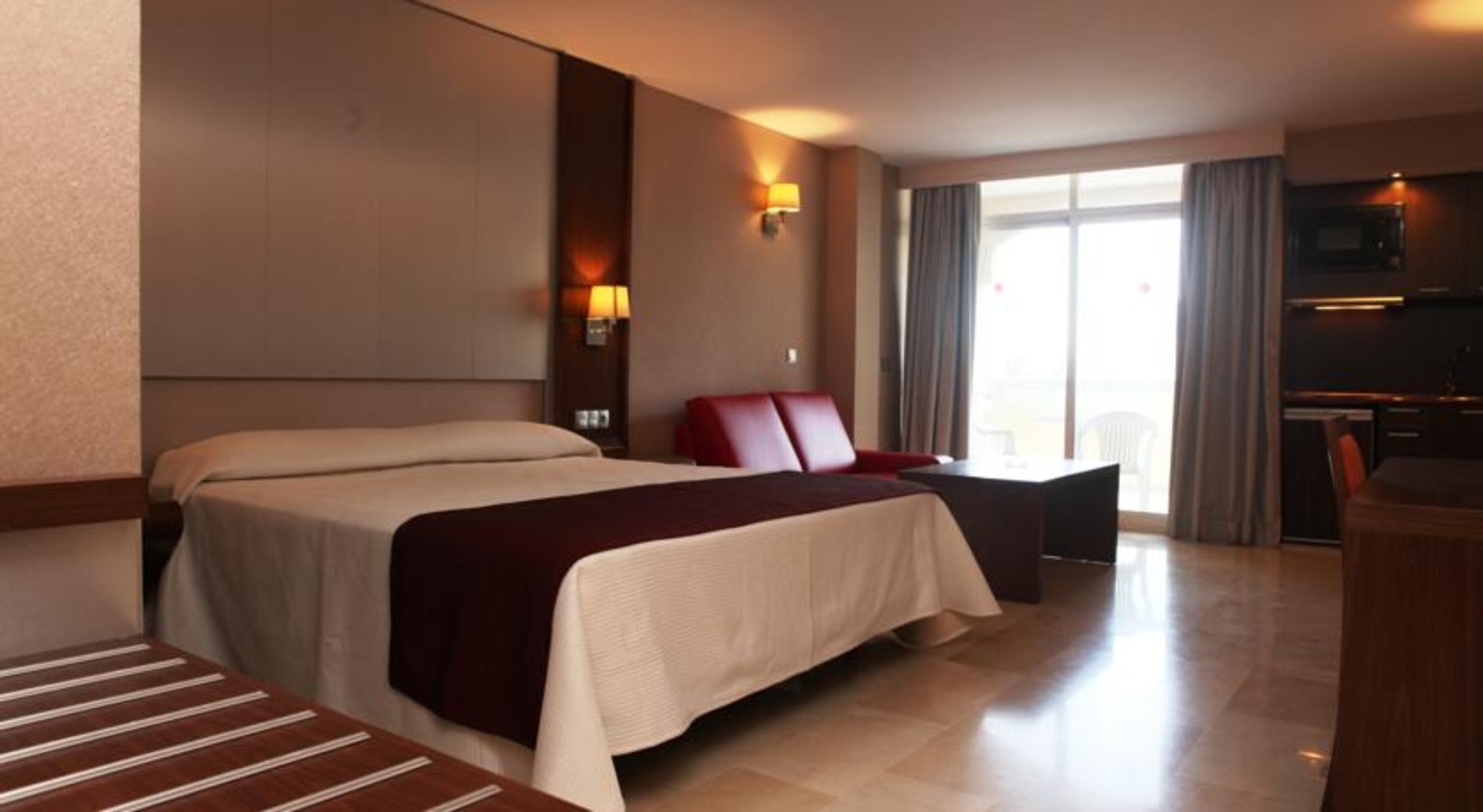 A hotel room with a large bed, a desk, a chair, and a TV.