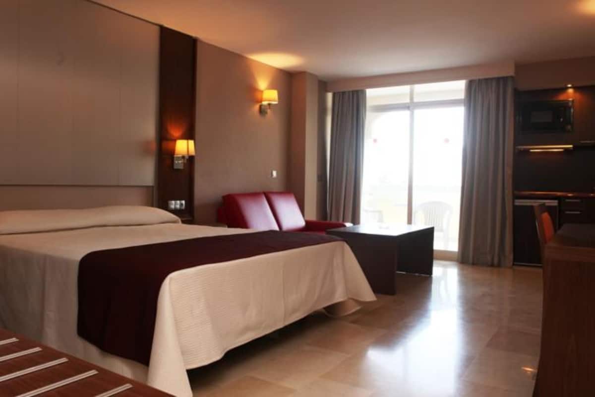 A hotel room with a large bed, a desk, a chair, and a TV.