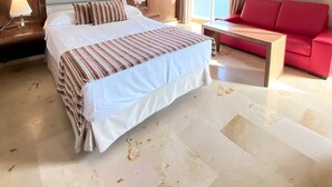 Habitación de hotel con una cama grande, un sofá rojo, una mesita y un ventanal con cortinas.