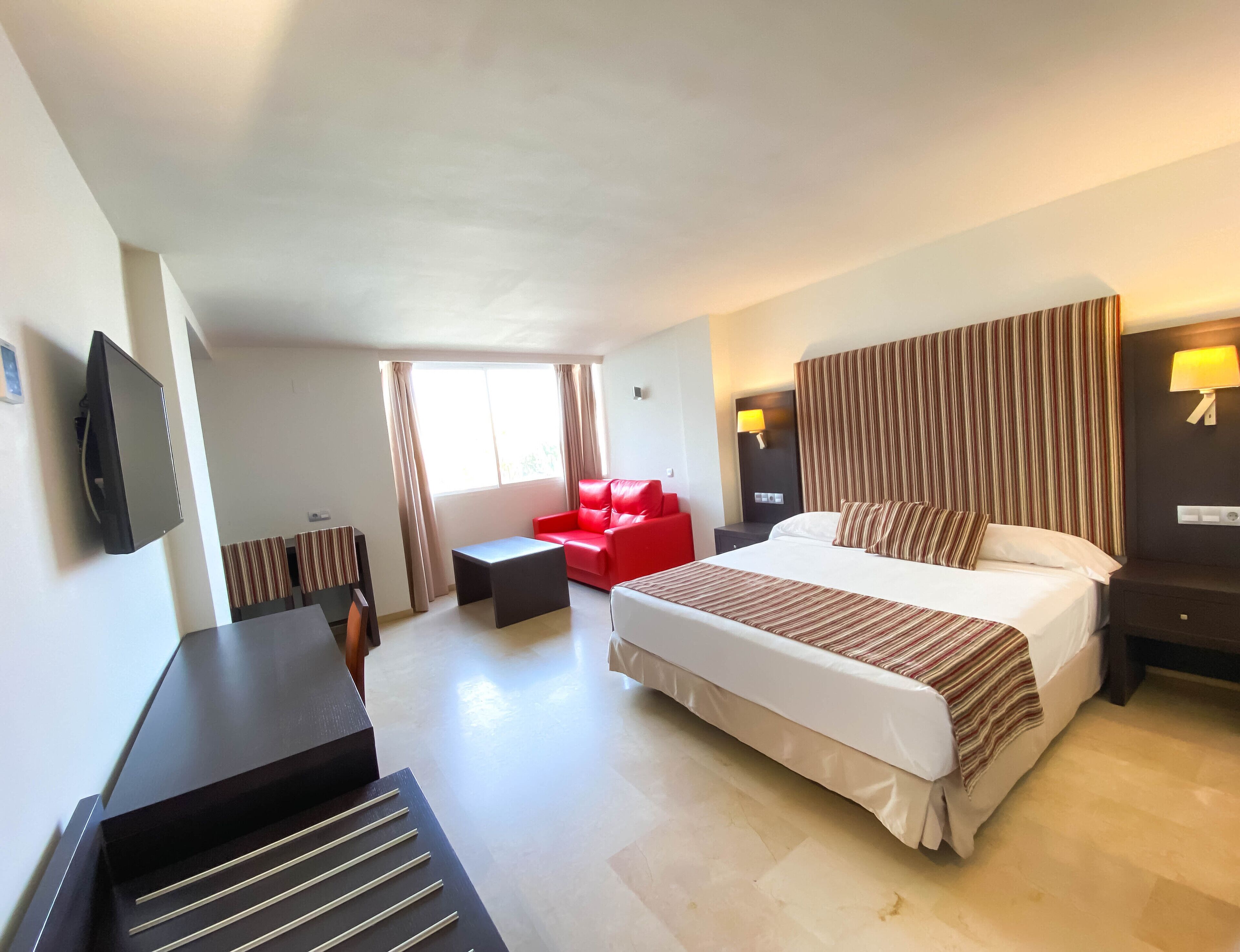 A hotel room with a bed, a red sofa, a desk, and a TV.