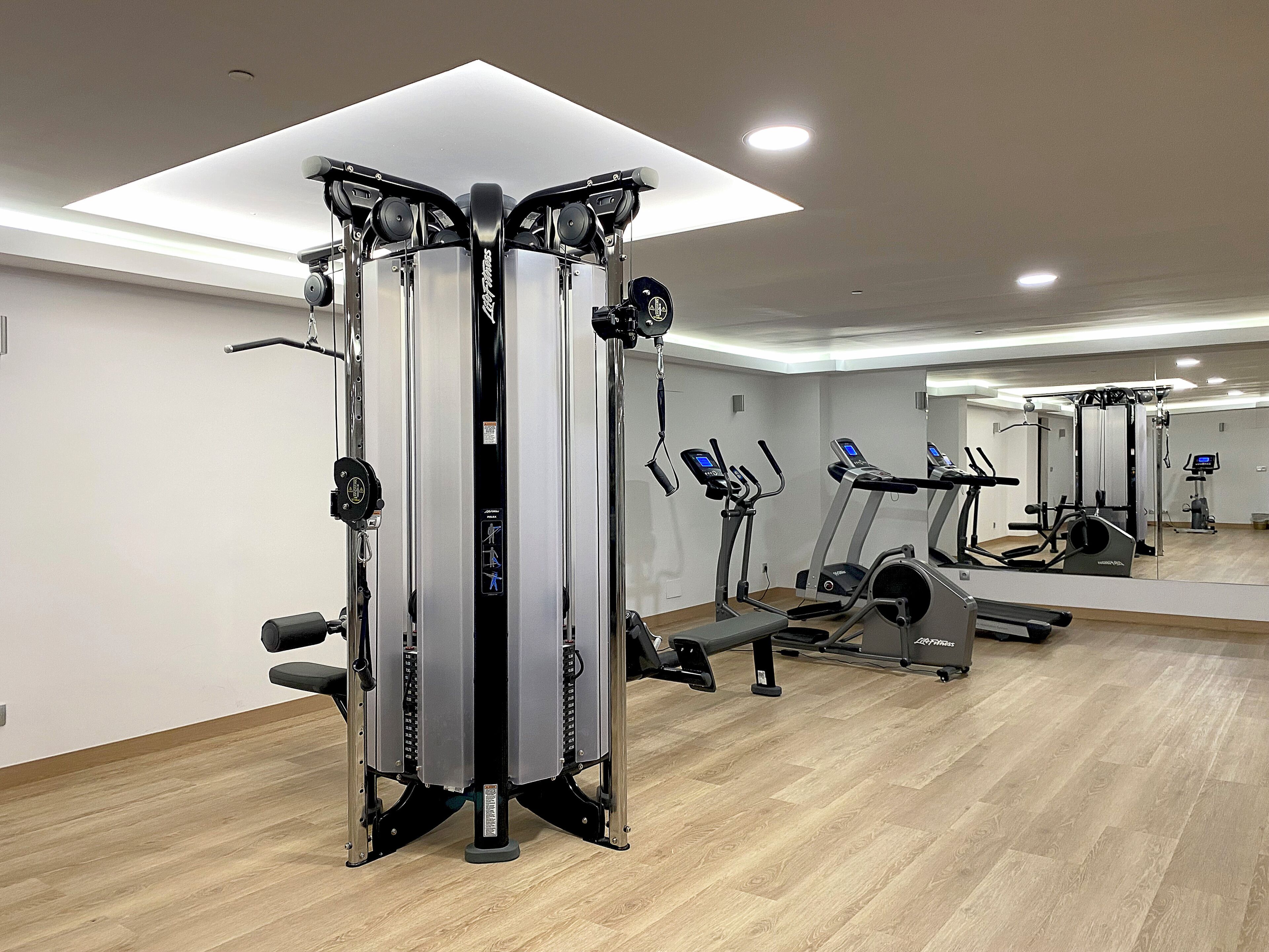 A modern gym with cardio machines, weight training equipment, and a large mirror.