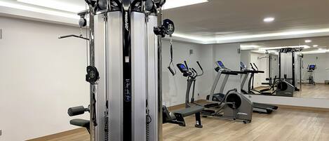 A modern gym with cardio machines, weight training equipment, and a large mirror.
