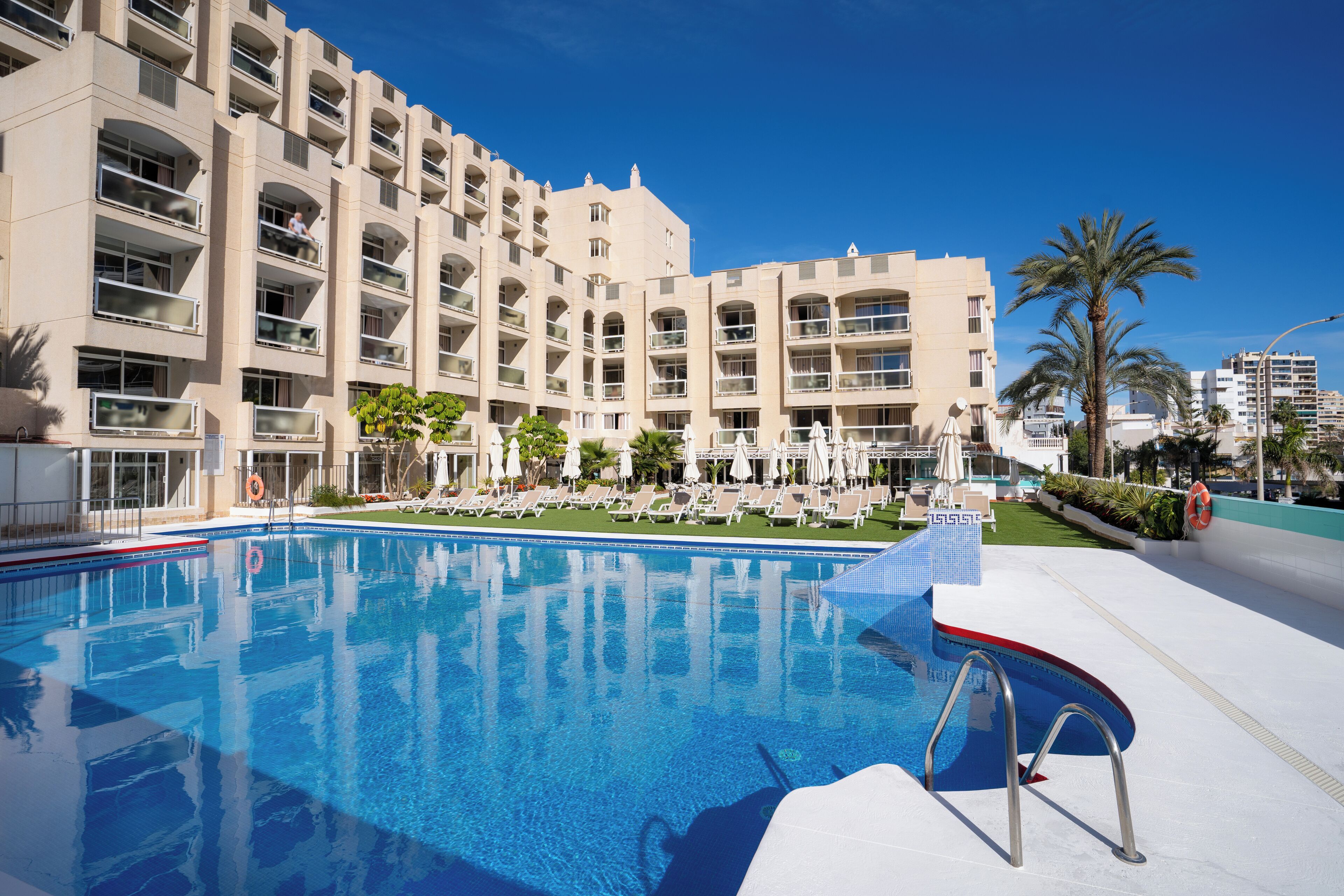 A hotel with a swimming pool, multiple balconies, and palm trees.