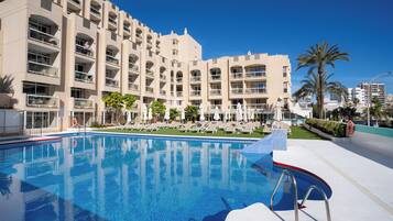 A hotel with a swimming pool, multiple balconies, and palm trees.