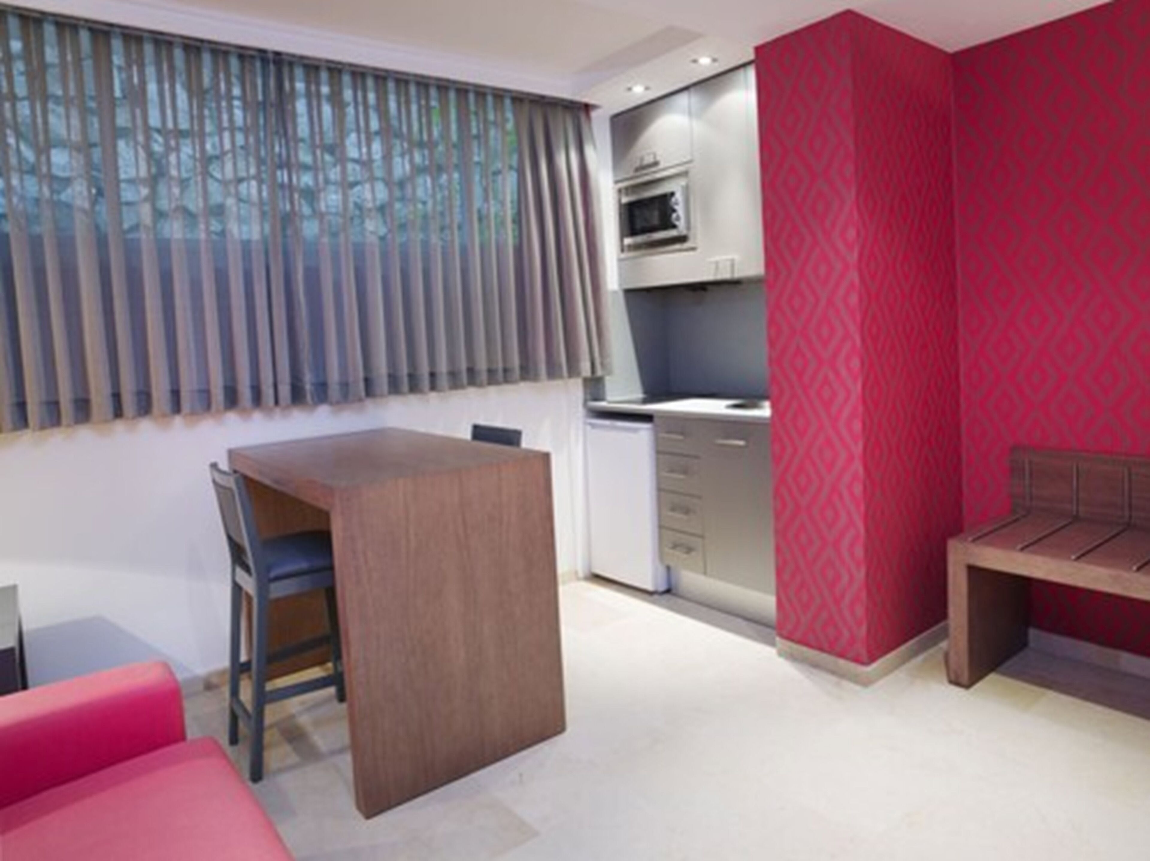 Una habitación compacta con kitchenette, comedor y una pared de acento roja.