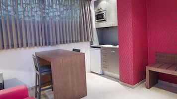 Una habitación compacta con kitchenette, comedor y una pared de acento roja.