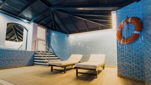 Zona de piscina con dos tumbonas, un flotador salvavidas y una escalera que lleva a un nivel superior.