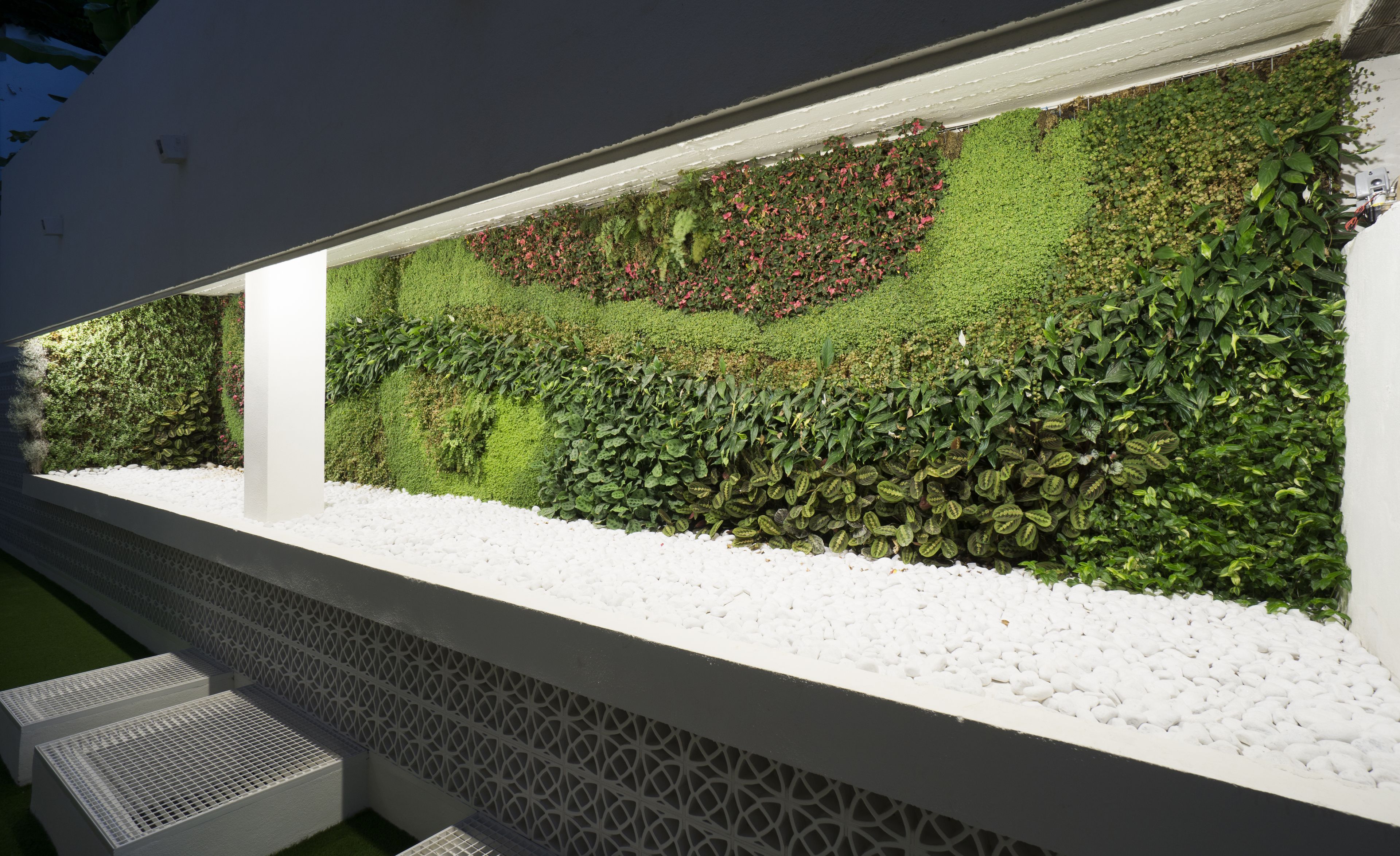 A modern building with a long, narrow garden area featuring a variety of plants and a white pebble border.